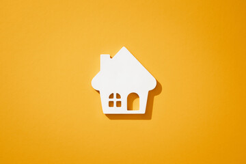 A white house model on yellow background, casting a subtle shadow.