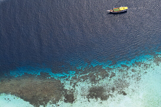 Aerial view of a boat drifting on the tranquil turquoise and deep blue waters near the coral reef, Pink Beach, East Nusa Tenggara, Indonesia.