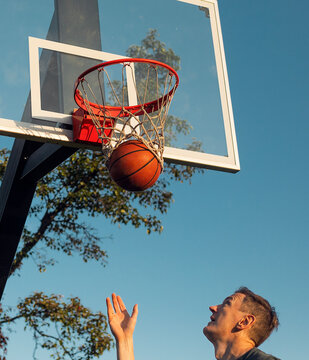 Man catches basketball from below hoop at sunset