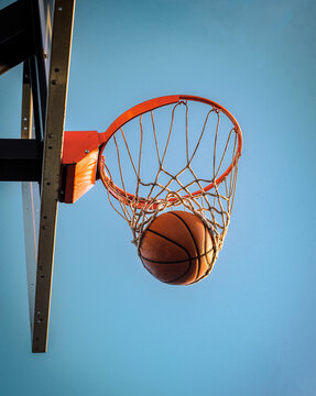 Basketball ball in a hoop against a blue sky