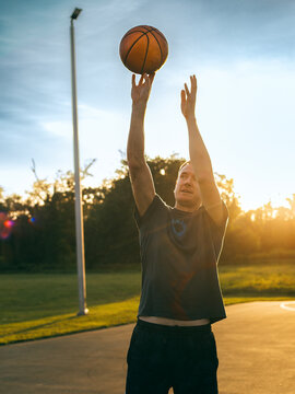 Man throws basketball in the rays of the setting sun