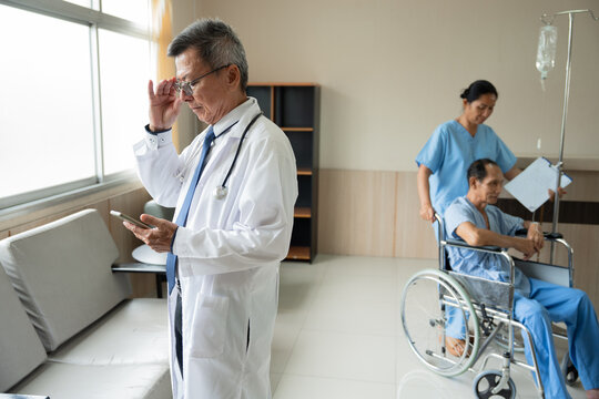 Doctor use smartphone with nurse take care patient old man with intravenous treatment in wheelchair background