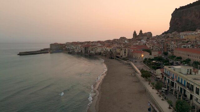 Aerial Drone Shot Flying Over The Coastal Town Of Cefalu And Beach In Sicily, Italy At Sunrise.