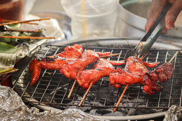 Grilled chicken wings on smoky charcoal grill, Thai street food scene with glossy red glaze, bamboo...