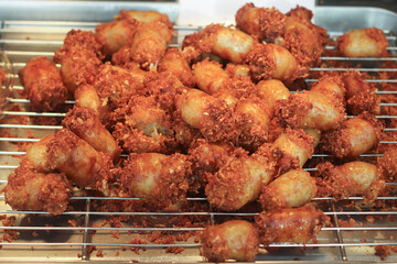 Crispy Thai fried fermented sausage, locally known as Naem, displayed on a street food stall tray. Golden texture and sour-savory flavor reflect authentic Thai street cuisine.
