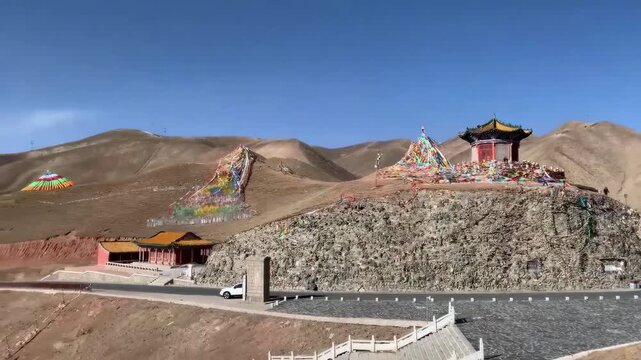 Colorful prayer flags and pavilion on a rocky hill at Sun Moon Mountain pass in Qinghai&rsquo;s Amdo region, with winding roads and dramatic Tibetan Plateau scenery.