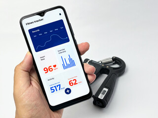 Close-up of a hand holding a smartphone displaying a fitness tracking app with workout stats and hand grip exerciser