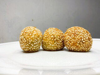 The traditional Indonesian food called onde onde sprinkled with sesame has a golden color and a round shape while placed on a white plate with a plain background
