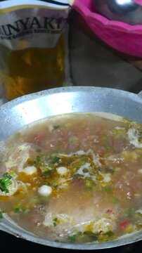 Homemade seblak cooking process with various toppings in a home kitchen. Popular Indonesian spicy street food prepared with authentic ingredients, flavorful seasonings, noodles, crackers, and assorted