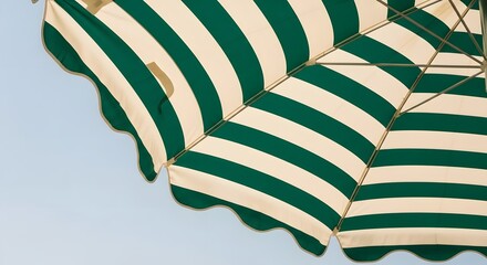 A vibrant green and cream striped umbrella with a scalloped edge providing shade against a clear blue sky.