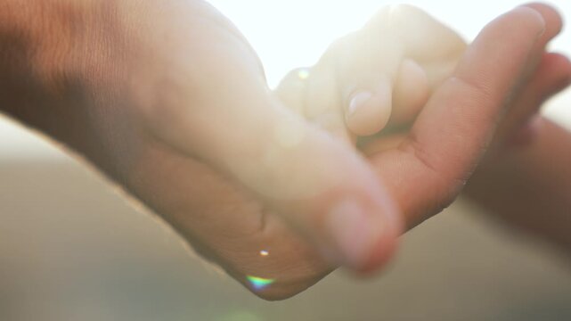 Holding baby finger with gentle hand parent palm cradles tiny finger in soft touch conveying love care tenderness protective bond between parent and child during quiet intimate connection warm glow
