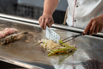 Chef stir frying fresh vegetables on a teppanyaki grill