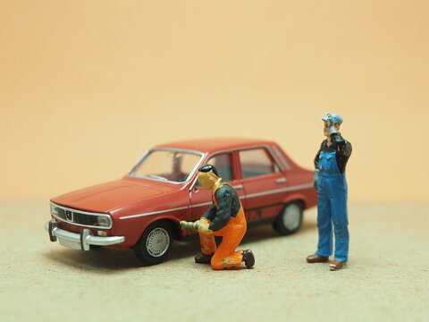 Mini toy of action figure at table with blurred background. Miniature photography concept design. Minifigure of mechanic crew character at garage with old car.