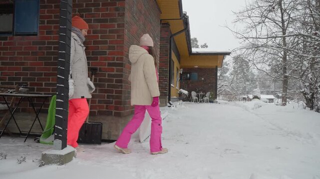 Mother and daughter shoveling snow at home during Christmas holidays. Winter tradition, festive lifestyle, outdoor activity, togetherness, bonding and seasonal joy in snowy yard.