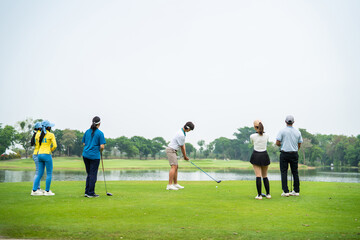 Group of young pro golfers swings their club on scenic golf course.