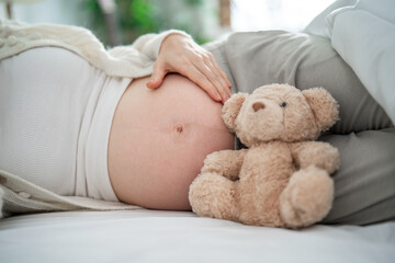 Close up of pregnant woman gently stroking belly while lying down on bed