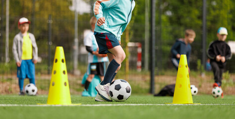 School boy dribbling soccer ball in slalom training drill. Football training camp for school kids. Soccer practice equipment on grass pitch