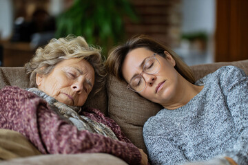 Elderly woman with dementia resting on sofa beside tired female caregiver, symbolizing caregiving challenges, natural indoor light