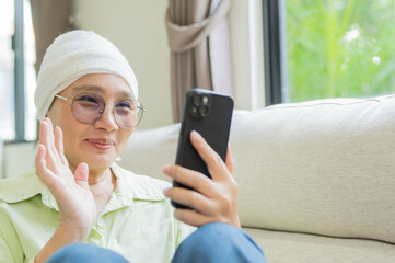 Woman in headscarf after chemotherapy using a mobile phone to greet her friends