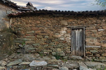Weathered stone wall of an old rural building with a rustic wooden door and traditional terracotta...