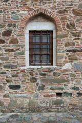Old stone and brick wall with an arched window, wooden frame, and metal bars. Rustic architectural detail of a historic building facade