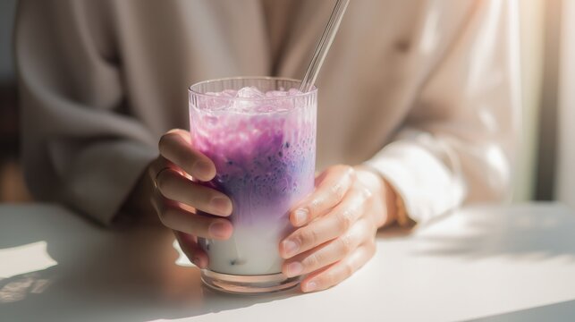 Woman holding glass of iced ube latte with reusable glass straw