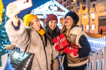Happy friends taking selfie at christmas market in the city at night