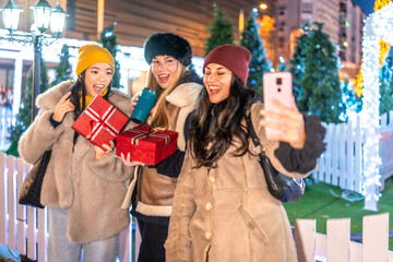Excited young women taking christmas selfie with gifts at night