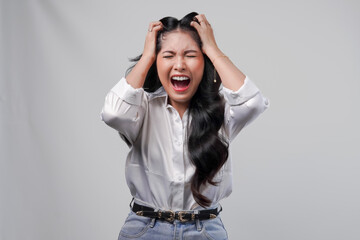Stressful young Asian woman in white shirt screaming and looking mad, isolated by white background.