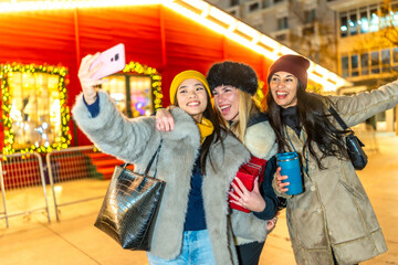 Cheerful friends taking selfie at christmas market in city at night