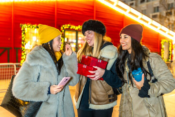 Happy women holding christmas gifts and enjoying christmas market at night