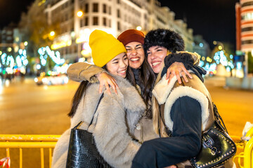 Happy friends embracing in a christmas city at night