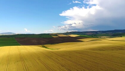 Obraz premium Rolling hills of farmland, sunlit fields, and a partly cloudy sky