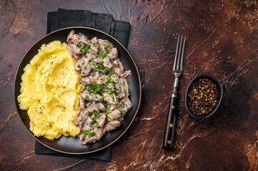 Beef stroganoff with mashed potatoes, fresh greenery and savory mushroom sauce in a plate . brown background. top view