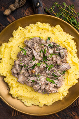 Beef Stroganoff over mashed potatoes with creamy sauce in a plate. wooden background. top view