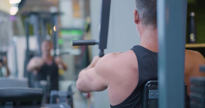 Gym workout. Butterfly exercise. Back view of a middle aged Caucasian man trains chest in the gym. Gym workout shows man targeting pectorals through butterfly machine exercise.