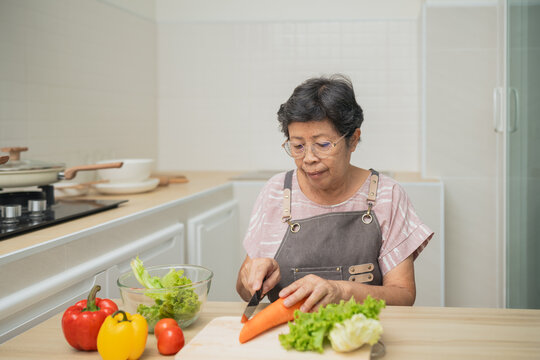Senior woman preparing fresh vegetables in a bright kitchen, focusing on a carrot with colorful peppers and lettuce on the counter