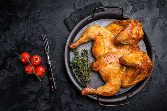 Roasted chicken Tabaka with herbs and spices, poultry meat on steel tray. black background. top view