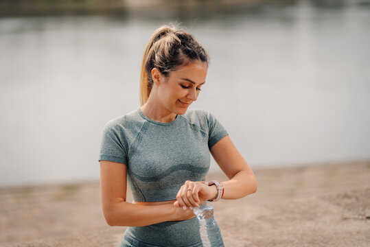 Sporty woman checking smartwatch near lake after exercising