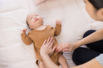Mother gently massaging baby tummy in bed