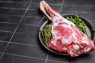 Uncooked whole lamb leg, raw mutton meat with herbs for cooking. black background. top view