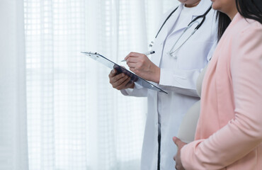 Doctor writing about health and symptoms of prenatal woman health on a medical chart for check up....