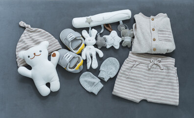 Flat lay of neutral-toned baby clothes and accessories on dark background, including plush toys,...