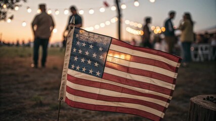 Independence celebration with American flag waving outdoors during family gathering holiday at sunset featuring blurred people and string lights