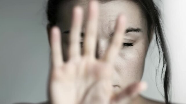 A woman with blue eyes raises her hand defensively, signaling stop. The expression on her face shows concern. Support the movement to prevent domestic violence. Displaying outrage against assault