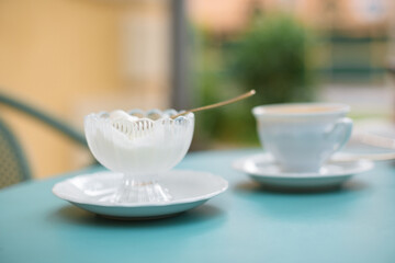 Vanilla ice cream in a glass bowl, a cup of cappuccino on a blue garden table on summer terrace.