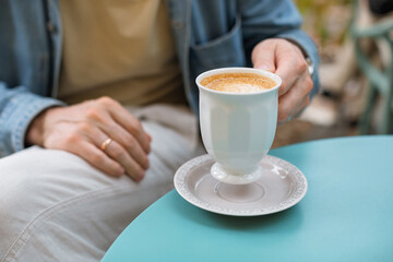 Close-up of a man enjoying coffee from an elegant, porcelain-white cup on a summer terrace.
