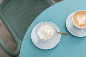 Vanilla ice cream in a glass bowl, a cup of cappuccino on a blue garden table on summer terrace.