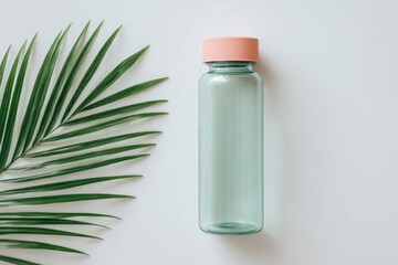 Aqua bottle with pink lid, beside a palm frond, centered on white background