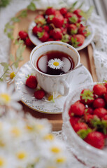 A cup of tea with a daisy floating on top is surrounded by fresh strawberries on a decorative tray. The scene radiates warmth and freshness, perfect for a sunny spring day